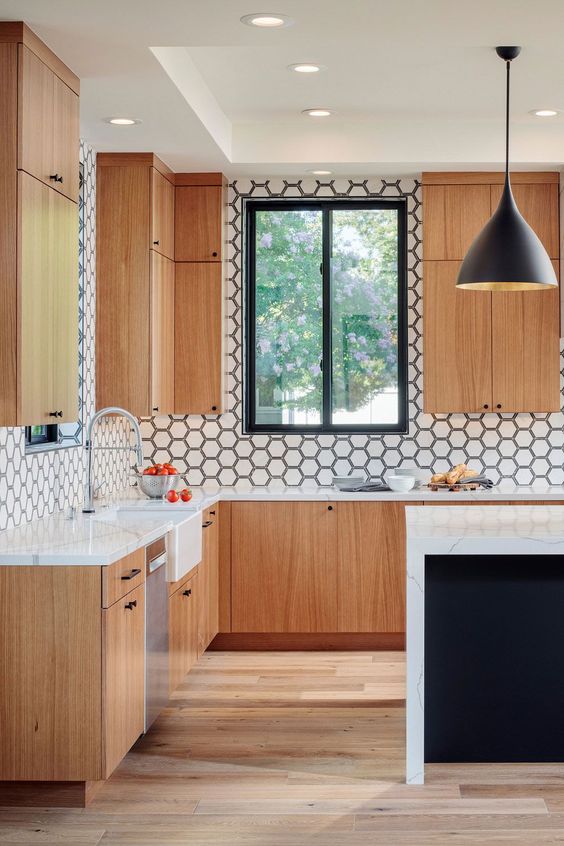 A cool modern kitchen with light stained flat panel cabinets, a white hex tile backsplash and a black kitchen island