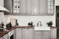 a cozy traditional grey kitchen with usual and glass cabinets, with rich-colored wooden countertops and metal knobs