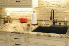 a creamy kitchen with shaker cabinets, a white tile and faux stone backsplash, built-in lights and a gold granite countertop that makes a statement