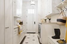 a creamy laundry mudroom with shaker cabinets, a hex tile floor, a bench with storage, a washing machine and a dryer and pendant lamps
