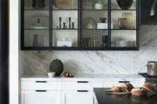 a dramatic black and white kitchen with shaker adn glass cabinets, a white kitchen island with a black countertop, a white backsplash