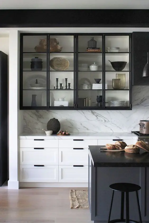 a dramatic black and white kitchen with shaker adn glass cabinets, a white kitchen island with a black countertop, a white backsplash