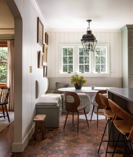 a farmhouse dining room with white shiplap walls, a built-in banquette seating, a round table and a terracotta tile floor