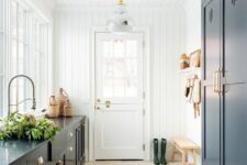 a farmhouse mudroom laundry with navy shaker cabinets, black countertops, a stained bench and glossy pendant lamps