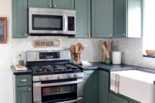 a green kitchen with shaker cabinets, black soapstone countertops and a neutral glossy tile backsplash plus stainless steel fixtures