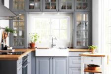 a grey kitchen with shaker and glass cabinets, butcherblock countertops, a tiny kitchen island and a window backsplash