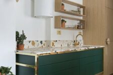 a hunter green kitchen island with gold touches and a bright terrazzo countertop and a backsplash looks very chic and bold