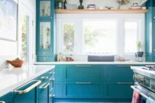 a lovely bright blue kitchen with shaker and glass front cabinets, white countertops, gold handles and a bold printed rug is wow
