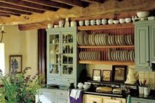 a lovely vintage kitchen with blue cabinets, a vintage hearth, open shelves for plates, wooden beams and a wooden dining set