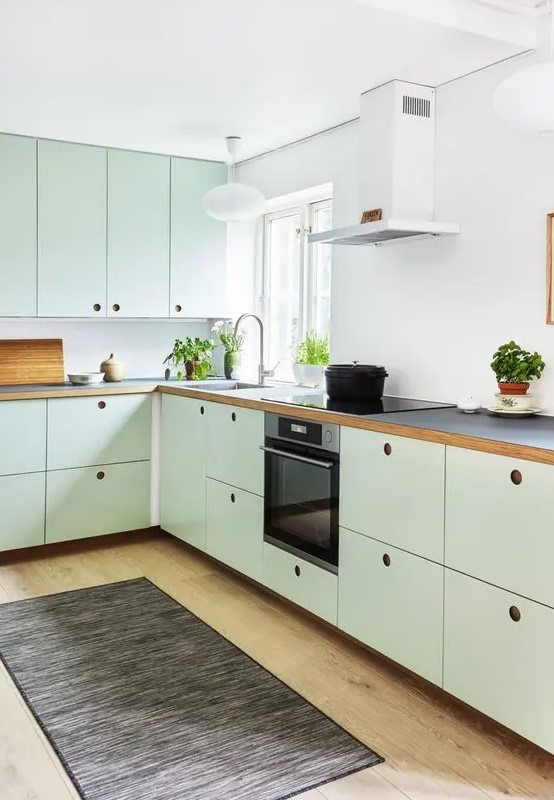A mint green kitchen with plywood cabinets, a white backsplash, black countertops, no handles and built in appliances