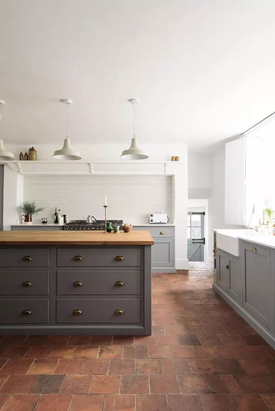 a modern farmhouse kitchen with lower grey cabinets and a large kitchen island, a terracotta tile floor and pendant lamps