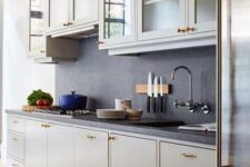 a modern grey kitchen with flat panel and glass front cabinets, black countertops and a backsplash, gold handles
