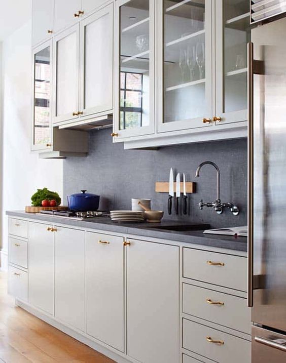 a modern grey kitchen with flat panel and glass front cabinets, black countertops and a backsplash, gold handles