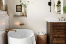 a modern rustic bathroom with white plaster walls and a terracotta tile floor, a stained vanity, an oval tub and greenery