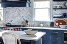 a navy kitchen with shaker cabinets, a neutral marble tile chevron backsplash, neutral granite countertops and tall stools