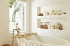 a neutral bathroom with white plaster walls with niches, a wabi-sabi tub, a terracotta floor, a white stool and baskets