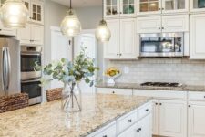 a neutral farmhouse kitchen with a neutral subway tile backsplash, tan granite countertops and pendant lamps