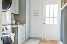 a pale blue mudroom entry with shaker cabinets, an open storage unit with baskets, printed rugs, a washing machine and a dryer