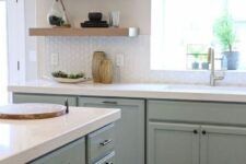 a sage green farmhouse kitchen with shaker cabinets, open shelves instead of upper cabinets, a large kitchen island and black fixtures