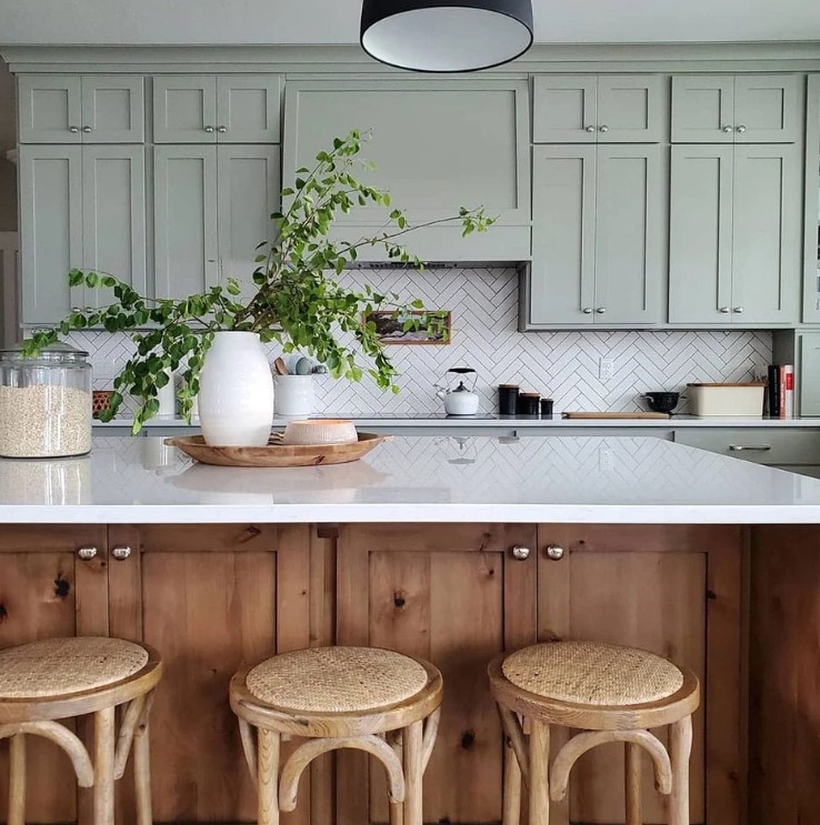 a sage green kitchen with shaker style cabinets, a herringbone tile backsplash, a stained kitchen island with a white countertop