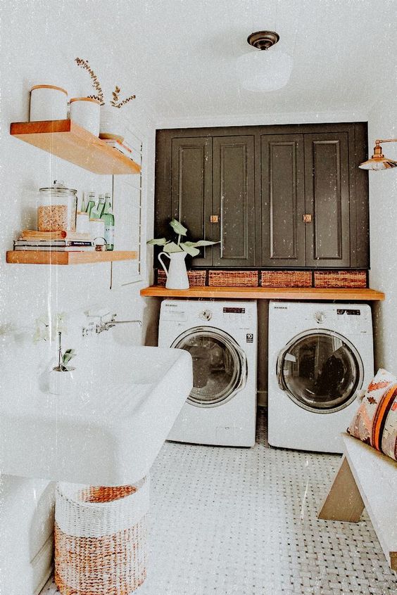a small mudroom laundry with black cabinets, a washing machine and a dryer, a floating sink and a bench with boho pillows