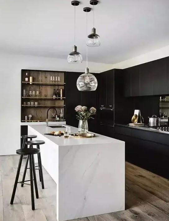 A stylish contrasting kitchen with sleek black cabinets, a white stone kitchen island, built in shelves and a cluster of pendant lamps