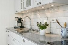 a stylish modern kitchen in white, with glossy tiles on the backsplash and grey granite countertops plus built-in lights is chic