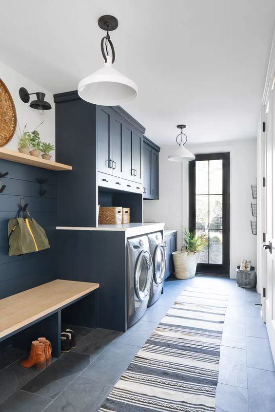 A stylish navy laundry mudroom with shaker cabinets, a washing machine and a dryer, a built in bench and an open shelf