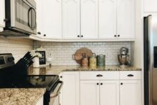 a stylish white kitchen with granite countertops, a white tile backsplash and black knobs and fixtures