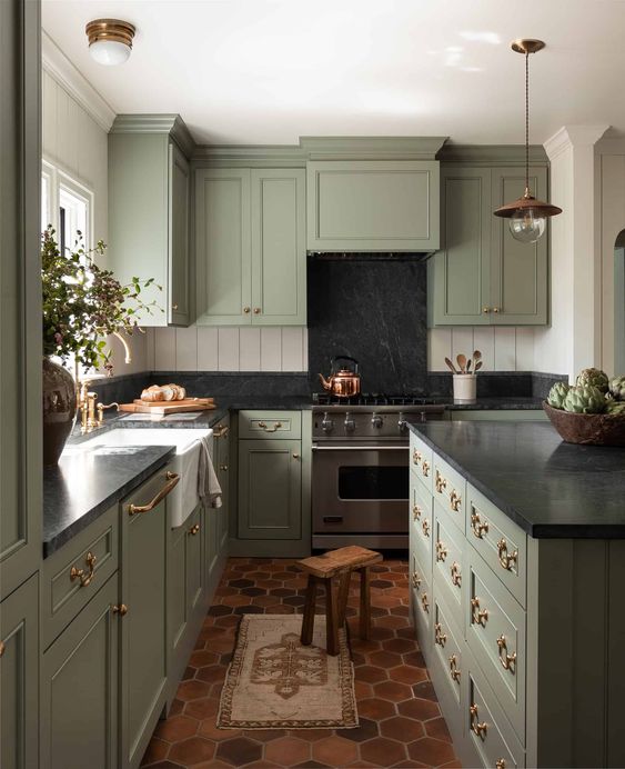 a vintage green kitchen with shaker style cabinets, black soapstone countertops and a backsplasj, white beadboard walls and pendant lamps