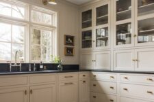 a vintage-inspired tan kitchen with shaker cabinets, black soapstone countertops, vintage fixtures and sconces