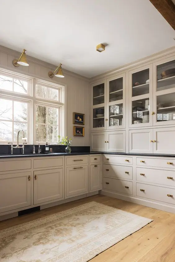 a vintage-inspired tan kitchen with shaker cabinets, black soapstone countertops, vintage fixtures and sconces