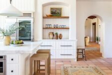 a white famrhouse kitchen with a terracotta tile floor, white shiplap cabinets, niches, a large kitchen island and pendant lamps