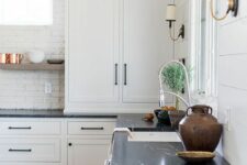 a white farmhouse kitchen with shaker cabinetry, black soapstone countertops, a white brick backsplash and open shelves