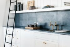 a white farmhouse kitchen with shaker cabinets, a black soapstone backsplash and countertops, open shelves and a black metal ladder