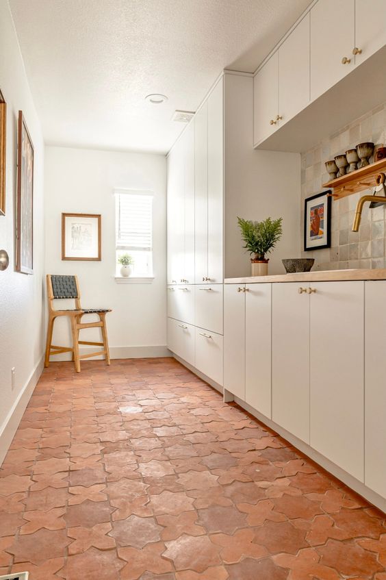 A white galley kitchen with sleek cabinets made more eye catchy with a terracotta tile floor, butcherblock countertops and artwork