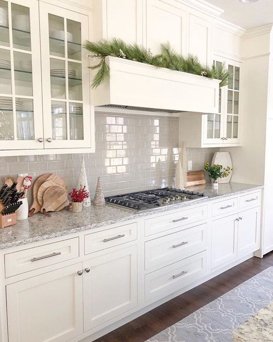 A white kitchen with shaker style cabinets, a grey tile backsplash, grey granite countertops and built in appliances