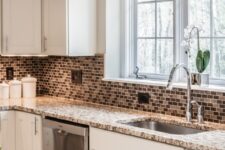 a white modern farmhouse kitchen with a tan small tile backsplash, beige and white granite countertops