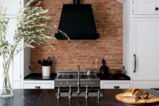 a white shaker style kitchen with a matching kitchen island, black soapstone countertops, elegant pendant lamps and dark stools