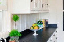 a white shaker style kitchen with a white beadboard backsplash, black soapstone countertops and black fixtures