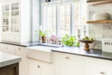 a white shaker style kitchen with black soapstone countertops, a white marble tile backsplash and open shelves