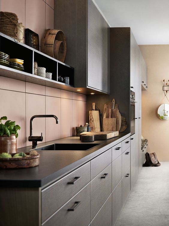 An elegant dark stained kitchen with black soapstone countertops and a matte pink tile backsplash plus black fixutres