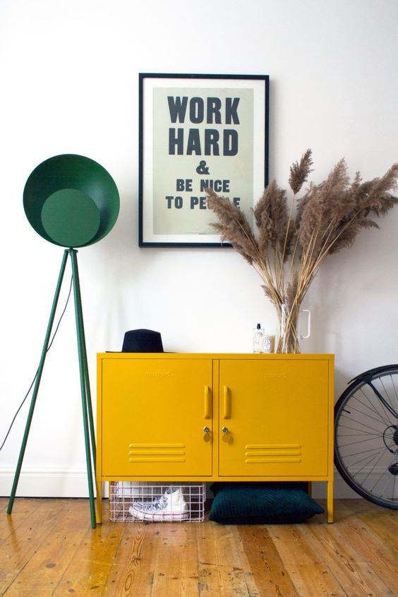 A mid century modern entryway with a mustard locker, pampas grass, a green floor lamp and a metal basket for storage