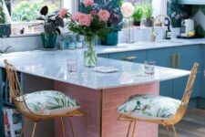 19 a blue kitchen with flat panel cabinets, bright blue and green floral wallpaper, white countertops and gold stools with bright pillows