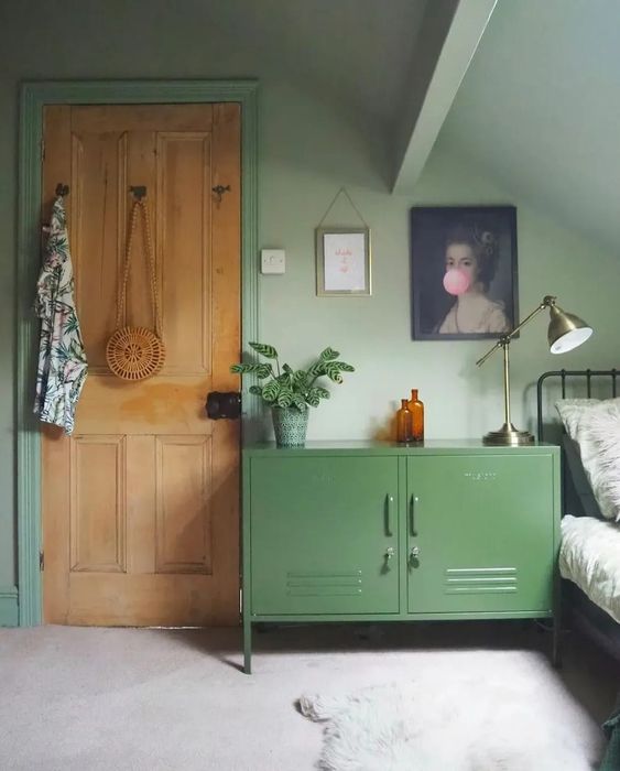 an attic green bedroom with a metal bed, a green locker as an alternative to a usual nightstand, some art and some gold touches