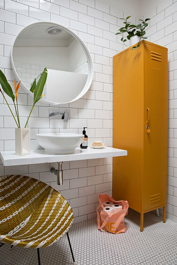 A catchy bathroom with white subway and hex tiles, a wall mounted vanity and sink, a mustard locker and a woven round chair