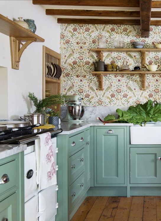 a green farmhouse kitchen with shaker cabinets, white stone countertops, delicate floral wallpaper, open shelves and potted greenery