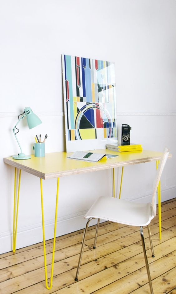 a sleek and delicate lightweight desk with neon yellow hairpin legs, a bold artwork, a blue table lamp and white chair