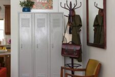 44 a mid-century modern mudroom with grey lockers, a mustard chair, a mirror in a dark-stained frame, a rack and some bright decor