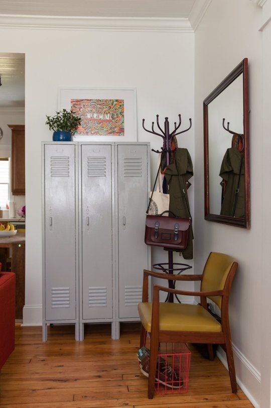 A mid century modern mudroom with grey lockers, a mustard chair, a mirror in a dark stained frame, a rack and some bright decor